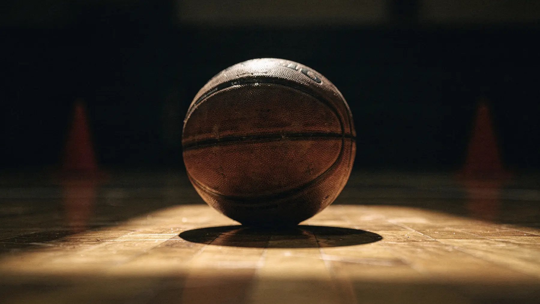 A basketball resting in a shaft of light on a hardwood court